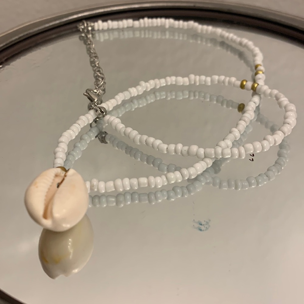 This a necklace with gold and white beads and a seashell on the end.